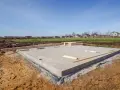 Betonowy fundament domu w budowie. Drewniane deski leżą na płycie. Rozważając budowa fundamentów cena, warto zobaczyć ten etap.