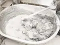 Mieszanie zaprawy z wapna palonego w dużej misie. Ręka w rękawicy miesza gęstą, szarą masę.