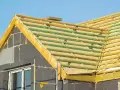 Drewniane łaty i kontrłaty tworzą konstrukcję pod przyszłe deskowanie dachu. Widać fragmenty ścian z oknem i izolacją.