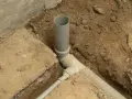 Wykop pod kanalizację z szarymi rurami PVC, częściowo zasypany ziemią.