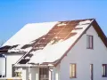 Biały dom pasywny z panelami słonecznymi na dachu, częściowo pokryty śniegiem.