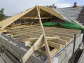 Trwa wymiana dachu. Widoczna drewniana konstrukcja więźby dachowej, materiały budowlane i fragmenty starego pokrycia.