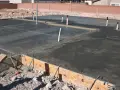 Świeżo wylany beton na budowie, widoczna izolacja pozioma fundamentów, rury i zbrojenie.