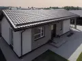 Nowoczesny dom z ceglaną elewacją i białymi tynkami, przykryty ciemnym dachem jednospadowym. Podjazd z kostki brukowej.