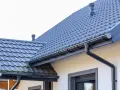 Szary dach z dachówki ceramicznej, rynny i komin. Sprawdź, jaka jest dachówka ceramiczna cena za m2.