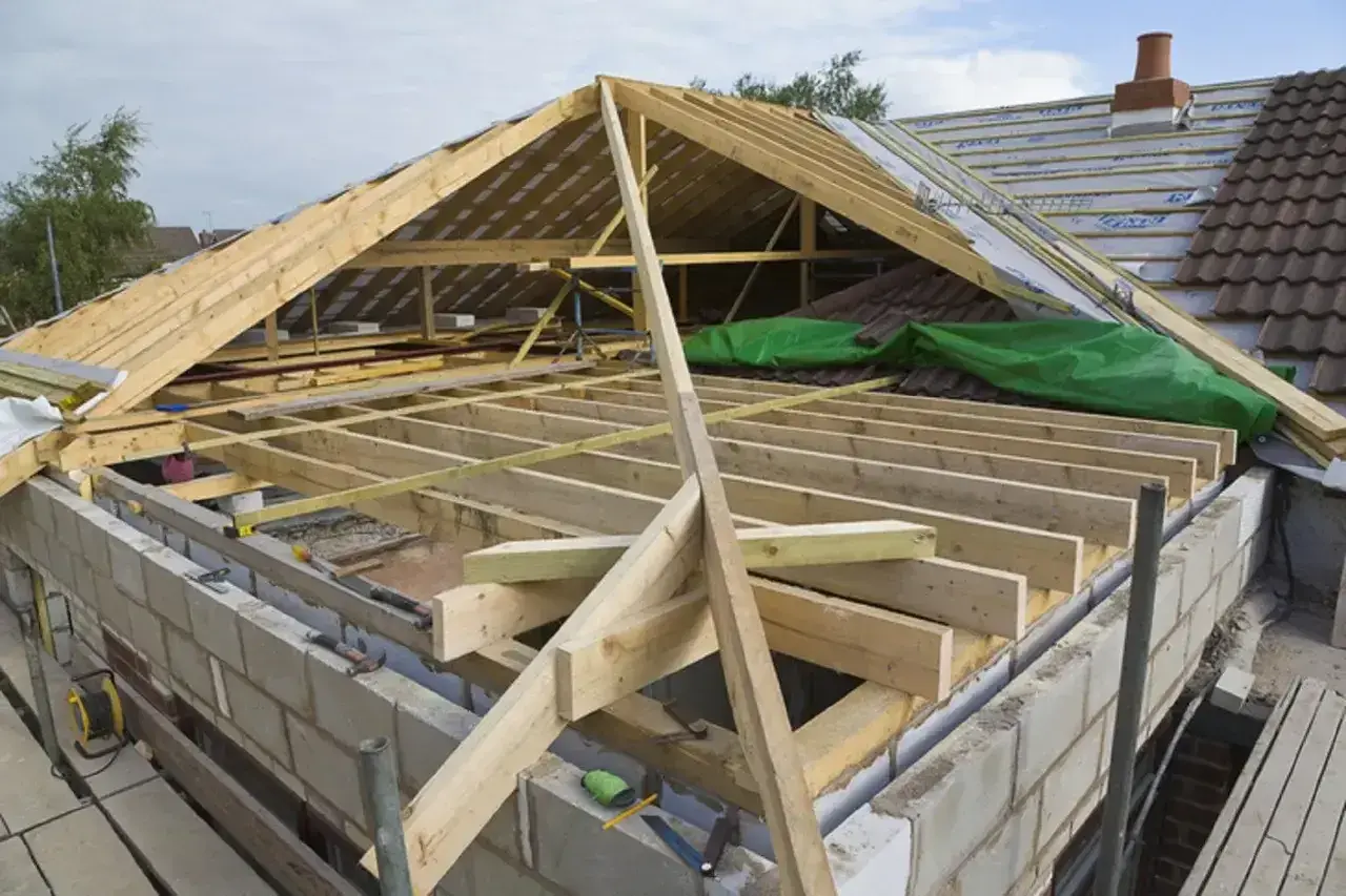 Trwa wymiana dachu. Widoczna drewniana konstrukcja więźby dachowej, materiały budowlane i fragmenty starego pokrycia.