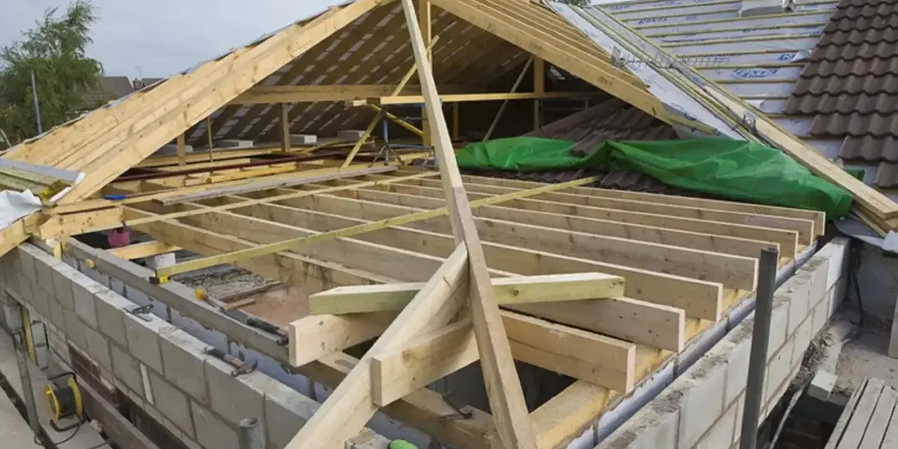 Trwa wymiana dachu. Widoczna drewniana konstrukcja więźby dachowej, materiały budowlane i fragmenty starego pokrycia.