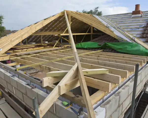 Trwa wymiana dachu. Widoczna drewniana konstrukcja więźby dachowej, materiały budowlane i fragmenty starego pokrycia.