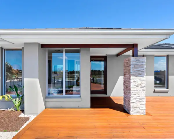 Nowoczesny dom z szarą elewacją, drewnianym tarasem i kamienną kolumną. Eleganckie, najmodniejsze kolory elewacji podkreślają jego styl.