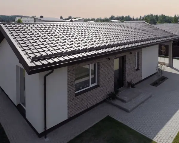 Nowoczesny dom z ceglaną elewacją i białymi tynkami, przykryty ciemnym dachem jednospadowym. Podjazd z kostki brukowej.