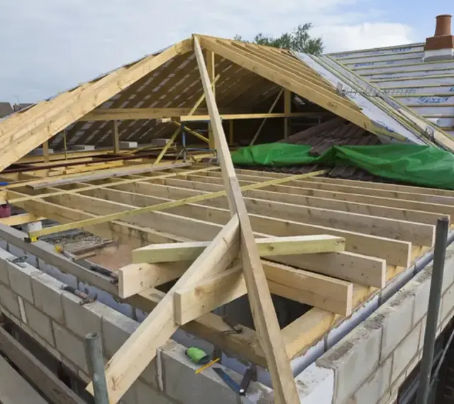 Trwa wymiana dachu. Widoczna drewniana konstrukcja więźby dachowej, materiały budowlane i fragmenty starego pokrycia.