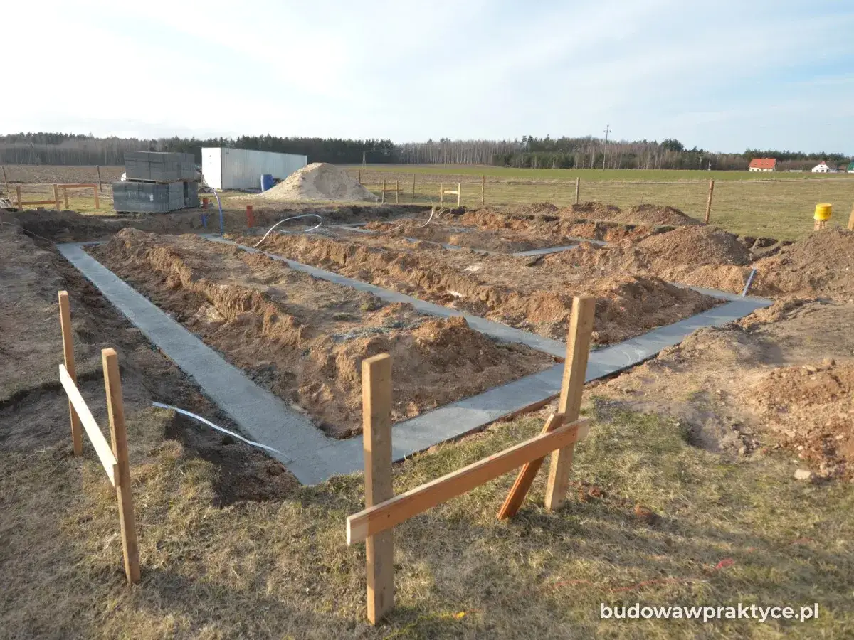 Wykonano ławy fundamentowe pod budowę domu. Widać wykopane rowy i wylany beton, przygotowane do dalszych prac.