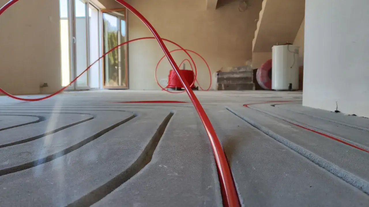 Instalacja ogrzewania podłogowego na podkładzie z anhydrytu. Czerwone rurki układane są w rowkach.