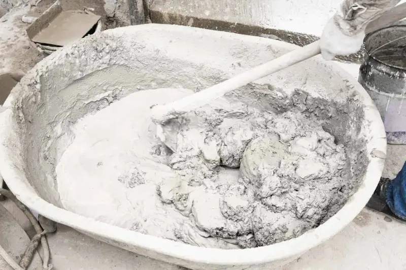 Mieszanie zaprawy z wapna palonego w dużej misie. Ręka w rękawicy miesza gęstą, szarą masę.